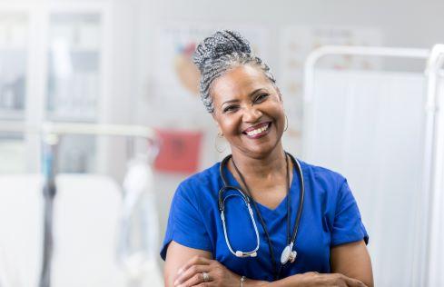 A smiling healthcare professional in blue scrubs with a stethoscope, in a medical setting, encouraging patients to make the right hospital choice.